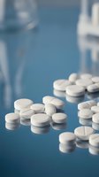 White pharmaceutical tablets scattered on blue surface with medical equipment in blurred background for healthcare and medicine concepts.