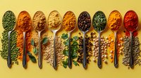 Colorful spices and herbs in vintage metal spoons arranged in row on yellow background. Fresh parsley leaves and peppercorns add natural accents to culinary composition.
