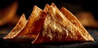 Golden crispy tortilla chips arranged in triangular stack on dark surface with warm lighting perfect for snack food advertising and restaurant menus.