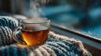 Steaming hot tea in glass mug with cozy knitted blanket by window on cold winter morning creating warm atmosphere for relaxation and comfort at home.