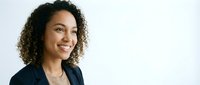 Happy mixed-race businesswoman with curly hair smiling confidently in professional blazer against white background for corporate marketing materials.