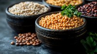 Raw legumes and pulses in rustic black bowls with chickpeas, lentils and beans. Fresh parsley garnish on dark background creates dramatic food composition.