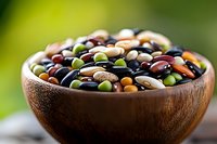 Colorful assortment of dried legumes and beans in wooden bowl against blurred green background, showcasing variety of plant-based proteins.