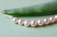 Lustrous pink pearl necklace resting beside a fresh green pea pod on a soft mint background, elegant jewelry concept.