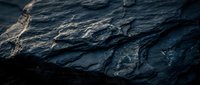 Dark blue slate rock surface with natural texture and golden light reflections creating dramatic shadows and highlights for backgrounds.