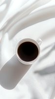 Cup of black coffee on white fabric with soft shadows, creating minimalist aesthetic for food and lifestyle content.