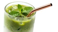 Iced matcha green tea latte in a glass with fresh mint leaves and a rose gold metal straw on white background.