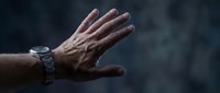 Mature man's open hand with wristwatch against dark background, expressing stop gesture, rejection, or refusal concept for communication and body language themes.