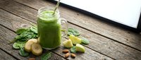 Fresh green smoothie in mason jar with spinach leaves, banana slices and almonds on rustic wooden table for healthy breakfast and detox nutrition.