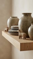 Ceramic vases with speckled glaze, stacked plates, and wooden elephant figurines arranged on floating wooden shelf for home decor styling.