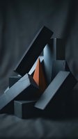 Abstract geometric composition with stacked black, gray, and rust-colored rectangular blocks arranged in dynamic balance against dark fabric backdrop. Suitable for modern design, branding, and contemporary art projects.