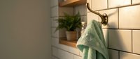 Modern bathroom interior with mint green towel hanging on brass hook near white subway tiles and wooden shelf with plant for home decor and wellness design.