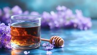Glass of honey tea with wooden dipper and fresh lilac flowers on blue rustic background. Aromatic herbal drink for relaxation and wellness.