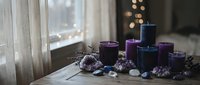 Purple and blue candles arranged with amethyst crystals on wooden table near window creating peaceful meditation and wellness atmosphere for relaxation.