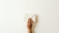 Mature woman's hand with gold bracelets holding paintbrush against white canvas on neutral background, artistic creation and creative expression concept.