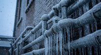 Frozen water pipes covered in thick ice and icicles during winter storm creating hazardous conditions for plumbing system maintenance and repair work.