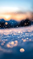 Magical winter sunset with glowing snow bokeh and golden light creating dreamy atmosphere. Blurred mountain silhouettes in background against orange sky.