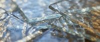 Cracked glass surface with sharp fragments and reflective shards creating abstract patterns. Broken window or mirror texture for safety concepts.