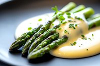 Fresh green asparagus spears served with creamy hollandaise sauce and chopped herbs on dark plate, close-up view with selective focus for food service.