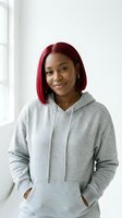 Young African American woman with red bob haircut wearing gray hoodie smiling confidently by window in bright modern interior for lifestyle content.