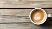 Fresh cappuccino with heart-shaped foam art in white ceramic cup on rustic wooden table background, top view with copy space for cafe menu design.
