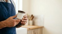 Male artisan holding ceramic jar with lid in kitchen workspace, showcasing handmade pottery and craft business branding for small business, retail, and product marketing.