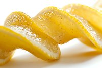 Fresh lemon peel spiral with textured zest and natural oils glistening on white background, macro close-up view showing citrus detail and culinary garnish.
