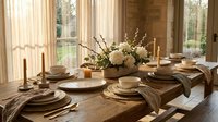 Elegant rustic dining table setting with natural wood plates, linen napkins, white flowers and warm sunlight streaming through windows.