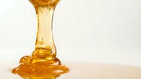 Golden honey dripping from spoon onto white surface, sweet liquid food ingredient for cooking, baking, and natural sweetener applications.