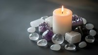 Burning candle surrounded by healing crystals and gemstones creating peaceful meditation atmosphere for wellness and spiritual practices.