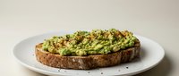 Smashed avocado toast topped with seeds and herbs on multigrain bread served on white plate, healthy breakfast or brunch meal for cafes and restaurants.