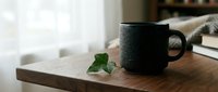 Dark ceramic coffee mug on wooden cutting board with fresh green ivy leaf in cozy kitchen setting with natural window light for morning routine concepts.