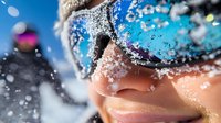Extreme close-up of snow-covered ski goggles reflecting winter mountain landscape, with snowflakes and frost on skin showing active winter sports lifestyle.
