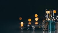Medical glass vials with metal caps and syringes on dark surface with warm bokeh lights creating professional healthcare atmosphere.