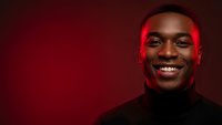 Happy young African American man smiling warmly in black turtleneck against red background with dramatic lighting for portrait photography.