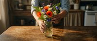 Florist arranging vibrant orange and purple flowers in glass vase on wooden table, suitable for floral design, greeting cards, and home decor projects.
