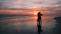 Romantic couple silhouette embracing on beach at sunset with golden sky and ocean waves reflecting on wet sand creating peaceful moment.