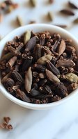 Aromatic whole cloves and cardamom pods in white ceramic bowl on marble surface, essential cooking spices for culinary and medicinal use.