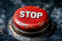 Red vintage stop button with worn metal texture and distressed paint on dark textured background, dramatic macro photography highlighting industrial details.