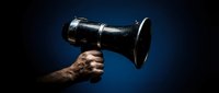 Hand holding vintage megaphone against dark blue background for communication and announcement concepts in business marketing campaigns.