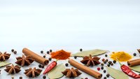Aromatic spices and herbs scattered on white background including cinnamon sticks, star anise, bay leaves, peppercorns, turmeric and chili peppers.