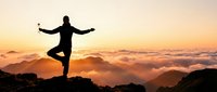 Silhouette of a person balancing on one leg atop a mountain at golden sunset, arms outstretched above a sea of clouds.