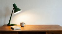 Wooden desk with green task lamp, stacked books, and ceramic mug in minimalist workspace setup for office, study, and interior design projects.