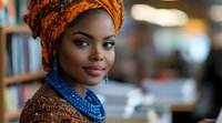 Young African woman wearing vibrant orange headwrap and traditional blue beaded necklace smiles confidently in soft natural lighting, showcasing cultural fashion and beauty.