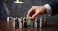 Businessman hand selecting green wooden figure from group of people. Human resources recruitment and team leadership concept for corporate hiring decisions.