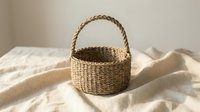 Handwoven natural wicker basket with handle on neutral linen fabric. Rustic home decor storage solution for organizing and styling modern interiors.