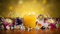 Spa wellness arrangement with burning candle, healing crystals, lotus flowers and baby breath on wooden surface for relaxation and meditation therapy.