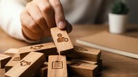 Hand placing wooden block with family icon onto stack of blocks with various symbols representing life planning and organization concepts on desk.