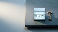 Lightbox sign with welcome message and vintage golden key on dark stone surface, symbolizing hospitality, new home, or real estate concept.