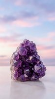 Purple amethyst crystal cluster on reflective surface against dreamy pastel sky background for spiritual healing and meditation practices.